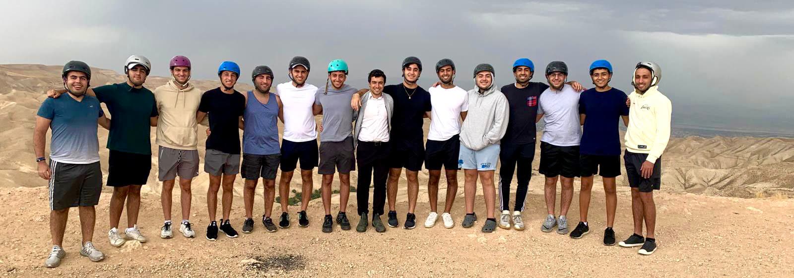 Rabbi Abergel and fifteen young men in helmets on a ridge in the Judean desert.