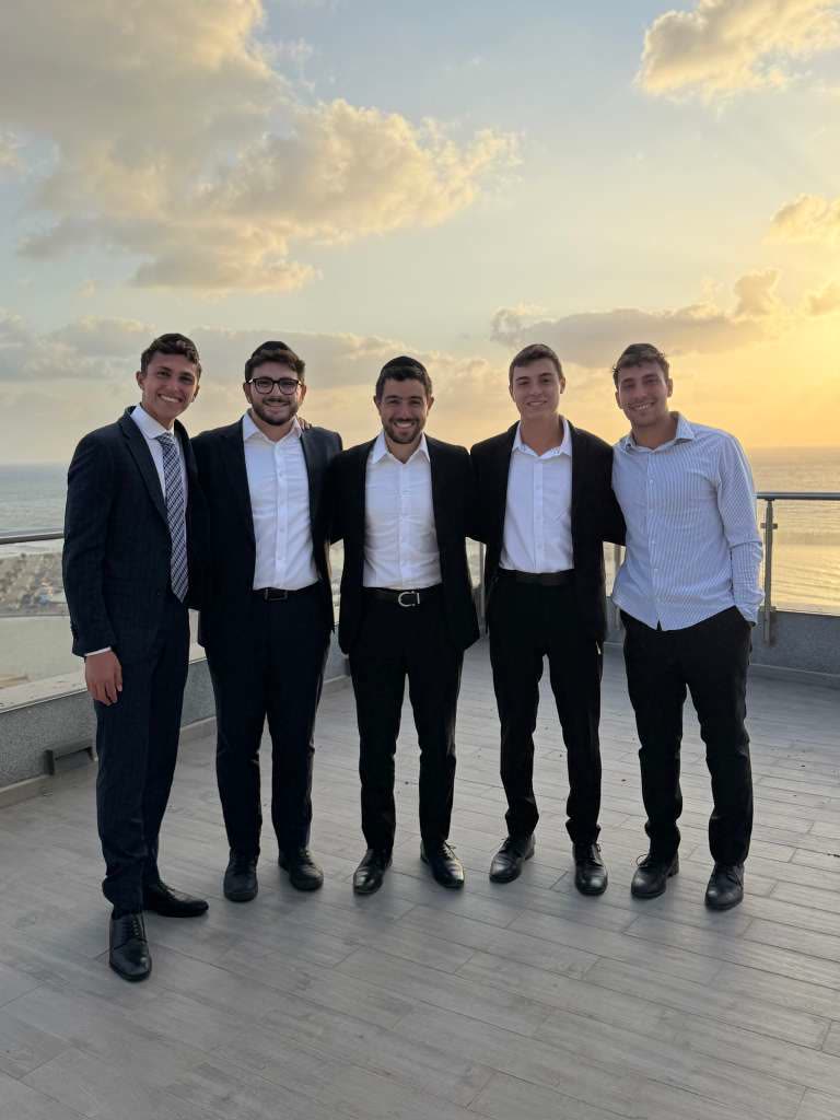 Rabbi Abergel with four young men on a rooftop at sunset, dressed for Shabbat.